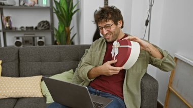 Kapalı koltukta dizüstü bilgisayar kullanırken kalp şeklinde hediye kutusu tutan sakallı gülümseyen adam..