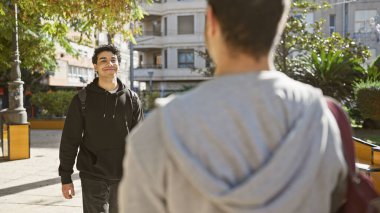 Çevresi yeşillik ve mimariyle çevrili, canlı bir şehir parkında arkadaşlıktan keyif alan iki İspanyol adam.