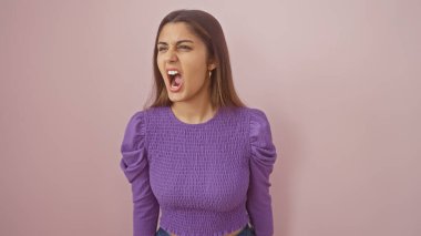 Öfkeli genç İspanyol kadın pembe izole bir arka planda çığlık atıyor, hayal kırıklığını ifade ediyor..