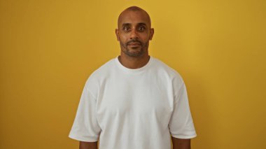 Young african american man standing over isolated yellow background, dressed in a white t-shirt, looking handsome and confident