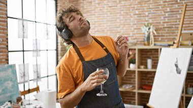 Stüdyodaki genç bir adam kulaklıkları ve bir bardak şarapla müzik dinlemeyi, rahatlamayı ve sanatsal yaşam tarzını benimsiyor..