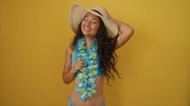 Sarı arka planda gülümseyen kolye ve şapkalı kadın, izole bir ortamda yakalanmış, yaz havasının somut bir örneği, neşeli bir ifade ve tropikal moda öğeleri..