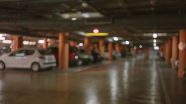 Blurred view of an indoor parking lot with defocused cars, columns, and lighting showcasing a bokeh effect and out of focus background. clipart