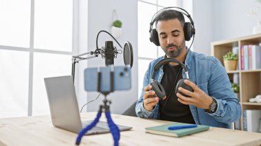 Stüdyoda sakallı, kulaklık takan ve ekipman kullanan İspanyol bir adam..