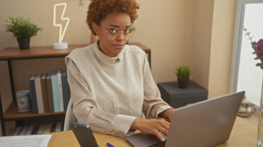 Modern bir ofis ortamında dizüstü bilgisayarla çalışan odaklanmış bir Afrikalı Amerikalı kadın..