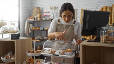 Bir pastanede çalışan kadın, kapalı bir mekanda tezgahı yönetirken vitrindeki hamur işlerine bakıyor..