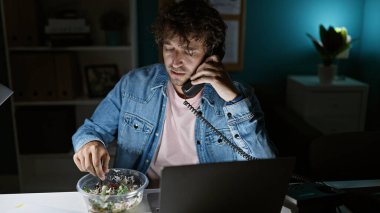 Genç İspanyol bir adam gece bir ofiste birden fazla iş yapıyor. Masasında salata yerken telefonla konuşuyor..