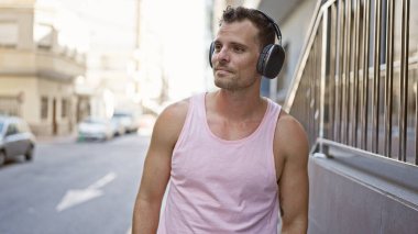 Kulaklıklı yakışıklı genç adam şehir korkuluklarının yanında duruyor, şehir yaşam tarzını ve modasını yansıtıyor..