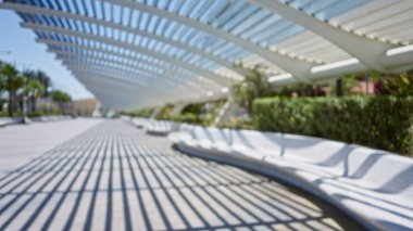 Arka planda mimari bir yapının ve palmiye ağaçlarının altında modern bir bank bulunan bulanık bir açık hava sahnesi.