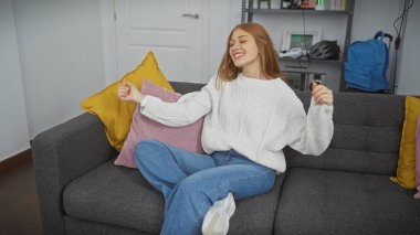 Neşeli bir kadın, rahat bir oturma odasındaki kanepede dans ederek rahatlar. Mutluluk ve rahatlığı ifade eder..