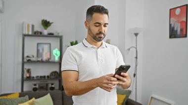 Modern oturma odasında akıllı telefon kullanan sakallı İspanyol bir adam.