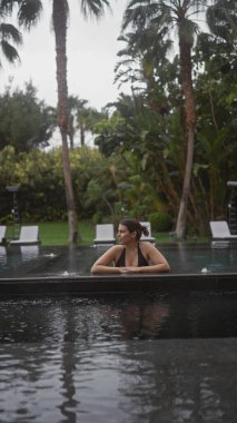 Genç bir kadın tropikal palmiyelerle çevrili sonsuz havuzda huzur içinde yaşıyor..