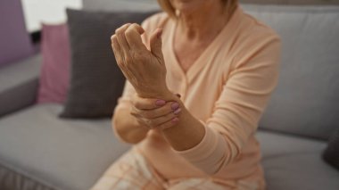 Olgun bir kadın evinde rahat bir oturma odasında otururken bileğini rahatsızlık içinde tutar..