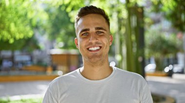 Yeşil şehir parkında gülümseyen yakışıklı genç adam..