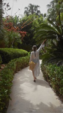 Yeşillik içinde, tropikal bir zarafet saçan genç bir kadının arka görüntüsü..