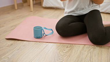 Evinde pembe yoga minderinin üzerinde uzanan genç bir kadının taşınabilir bir hoparlörle çekilmiş görüntüsü..