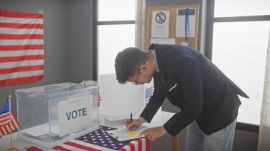 Takım elbiseli genç bir İspanyol, Amerikan bayraklarıyla süslenmiş bir oy kullanma merkezinde oy pusulasına yazmak için eğilmiş..