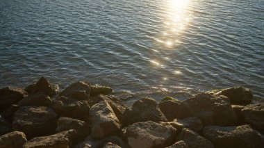 Sakin bir gün doğumu sakin göl suyuna yansıyor kayalık kıyı şeridi önplanıyla, sakin bir açık hava manzarası yaratıyor..