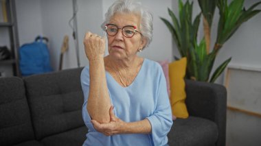 Oturma odasında dirseğini tutarak acı içinde kıvranan yaşlı bir kadın..