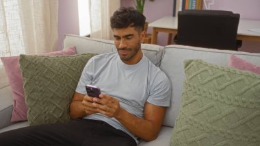 Evdeki kanepede rahat bir oturma odasında cep telefonu kullanan genç bir İspanyol.