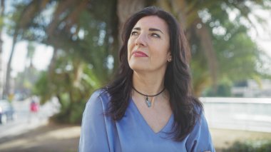 Kendinden emin, olgun İspanyol kadın güneşli bir şehir parkına bakıyor..