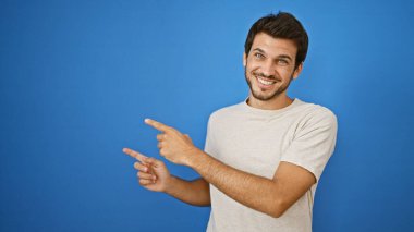 Sakallı, açık havada mavi bir arka plana bakıp gülümseyen neşeli, genç bir İspanyol.