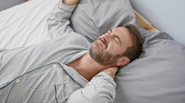 Orta yaşlı, sakallı, evde yatıp boynunu sıkan İspanyol bir adam..