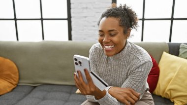 Samimi bir apartman dairesinde elinde kredi kartı ve akıllı telefon tutan gülümseyen kadın.