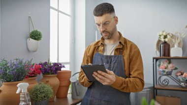 Sakallı, gözlüklü ve önlüklü yakışıklı. Çiçekçide tablet kullanıyor.