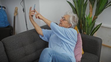 Son sınıf öğrencisi kadın rahat oturma odasındaki kanepede selfie çekiyor, modern, yaşlı yaşam tarzını somutlaştırıyor..