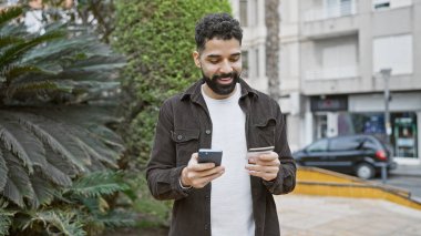 Sakallı, sakallı, şehir caddesinde elinde akıllı telefon olan yakışıklı, yetişkin bir adam..