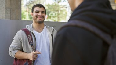 İki adam şehir ortamında konuşuyor, biri gülümsüyor, rahatlatıcı, dostane bir atmosfer yaratıyor..