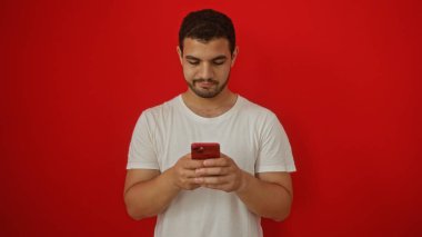Beyaz gömlekli, izole edilmiş kırmızı arka planda akıllı telefon kullanan yakışıklı bir İspanyol.
