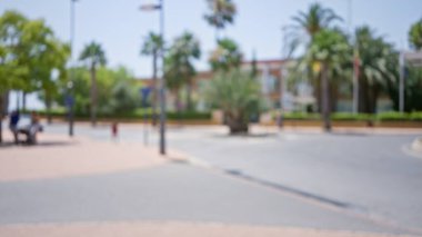 Açık hava sahnesi bulanık. Arka planda ağaçlar ve banklarda oturuyorlar. Güneşli bir gökyüzünün altında.