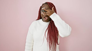 Süslü, beyaz bir kazakla pembe bir arka plana karşı poz veren, neşeli bir ifadeyi canlandıran şaşırmış Afrikalı bir kadın..