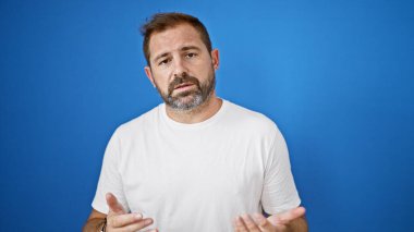 Beyaz saçlı olgun İspanyol bir adam mavi bir duvarın karşısında duruyor, açık havada bir konsept sunuyor..