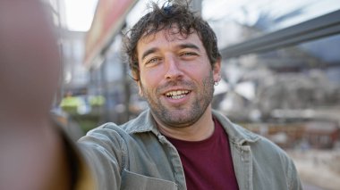 Yakışıklı İspanyol bir adam kalabalık bir şehir sokağında özçekim için gülümsüyor, günlük tarzını sergiliyor ve açık havada neşeli bir an yaşıyor..