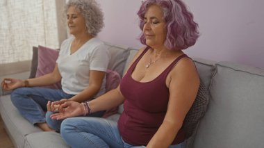 Orta yaşlı kadınlar evlerinin oturma odasında birlikte meditasyon yapıyorlar..