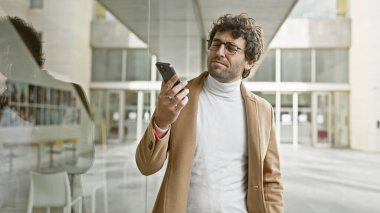 Gözlüklü ve sakallı İspanyol bir adam şehirde akıllı telefon kullanıyor..