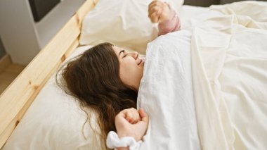 Genç bir İspanyol kadın yatakta gülümsüyor, rahat bir evde güzellik ve sükunet yayıyor..