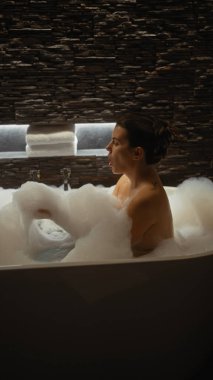 Genç bir İspanyol kadın, loş bir duvarla çevrili bir banyoda köpüklü bir banyoda dinleniyor, sükuneti ve kendine bakımı somutlaştırıyor..