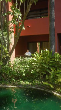 Genç bir kadın, yemyeşil ve dingin bir havuz ile çevrili bir bali tatil köyü terasında sükunetin tadını çıkarıyor..