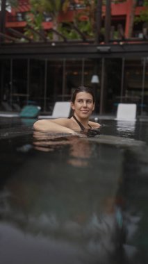 Gevşemiş bir İspanyol kadın, bale tatil köyü yüzme havuzunda sükunetin tadını çıkarıyor. Rahatlık ve zarafetin vücut bulmuş hali..