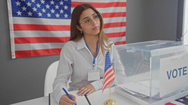 A young hispanic woman in a white coat oversees an electoral ballot box in a room with the american flag. clipart