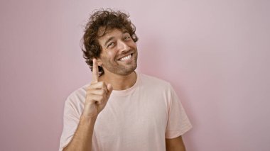 Yakışıklı, gülümseyen ve yukarıyı gösteren genç bir adam, pembe bir arka planda soyutlanmış.