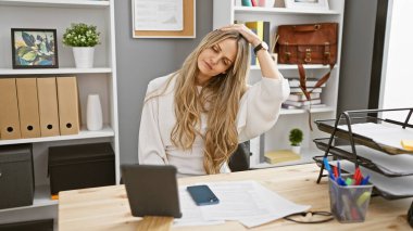 Sarışın kadın, modern ofis masasında dokümanlar ve akıllı telefonlarla rahatlıyor ve gündelik iş hayatı sergiliyor..