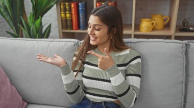 Gülümseyen İspanyol kadın, sıcak oturma odasında el hareketleriyle sunum yapıyor.