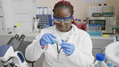 Laboratuvar önlüğü ve güvenlik gözlüğü takan Afrikalı Amerikalı kadın laboratuarda araştırma yapıyor.