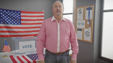 Olgun bir adam, Amerika 'da bir seçim merkezinde Amerikan bayrağı ve oy sandığıyla duruyor. Demokrasi ve vatanseverlik sergiliyor..