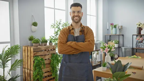 stock image Smiling bearded man with crossed arms in apron standing inside a lush flower shop.